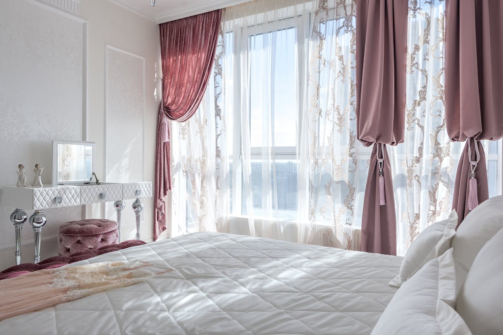 Bright, elegant bedroom with chic decor, featuring pink drapes and a comfortable bed, exuding luxury and style.
