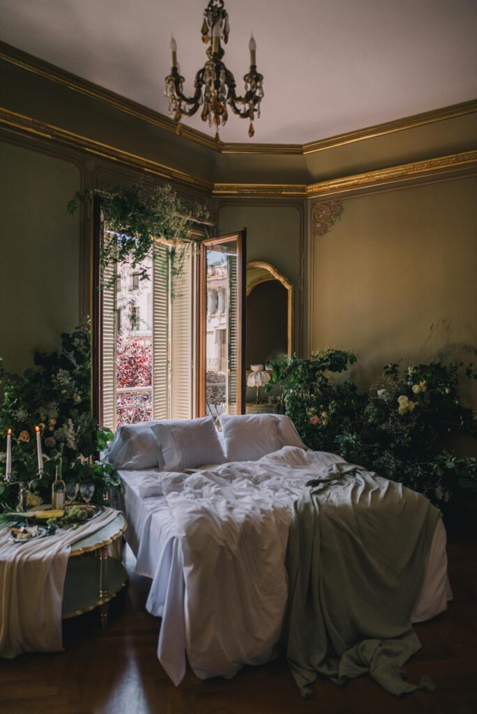 Elegant vintage bedroom with plants, luxurious decor, and ample natural light from windows.