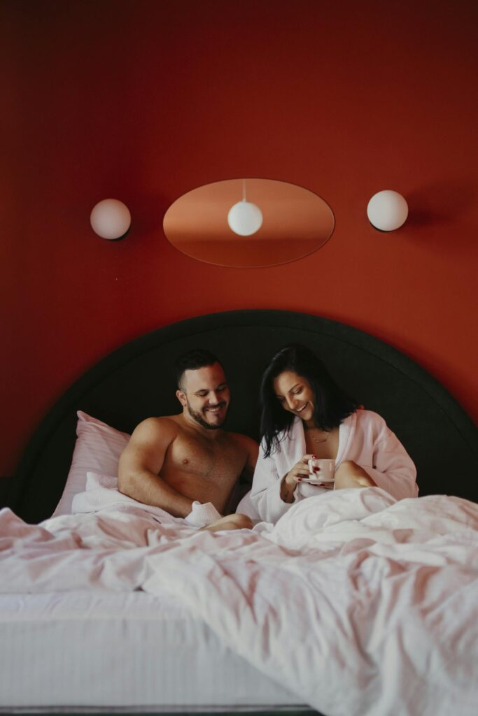 Happy couple enjoying cozy morning in bed with red background and warm lighting.